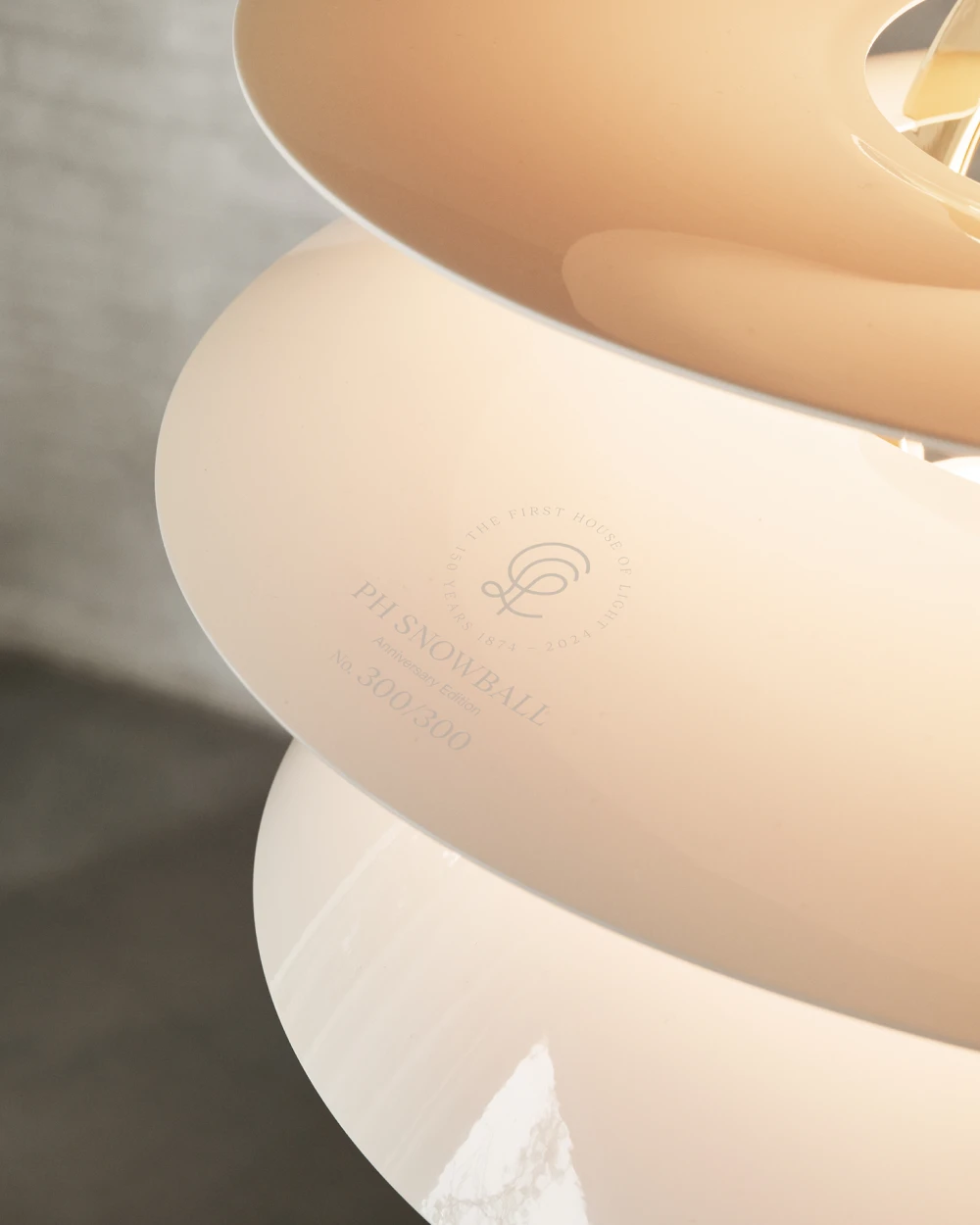 Close-up of the white PH Snowball pendant, showing its engraved anniversary mark and warm glow. © 2026 Louis Poulsen.