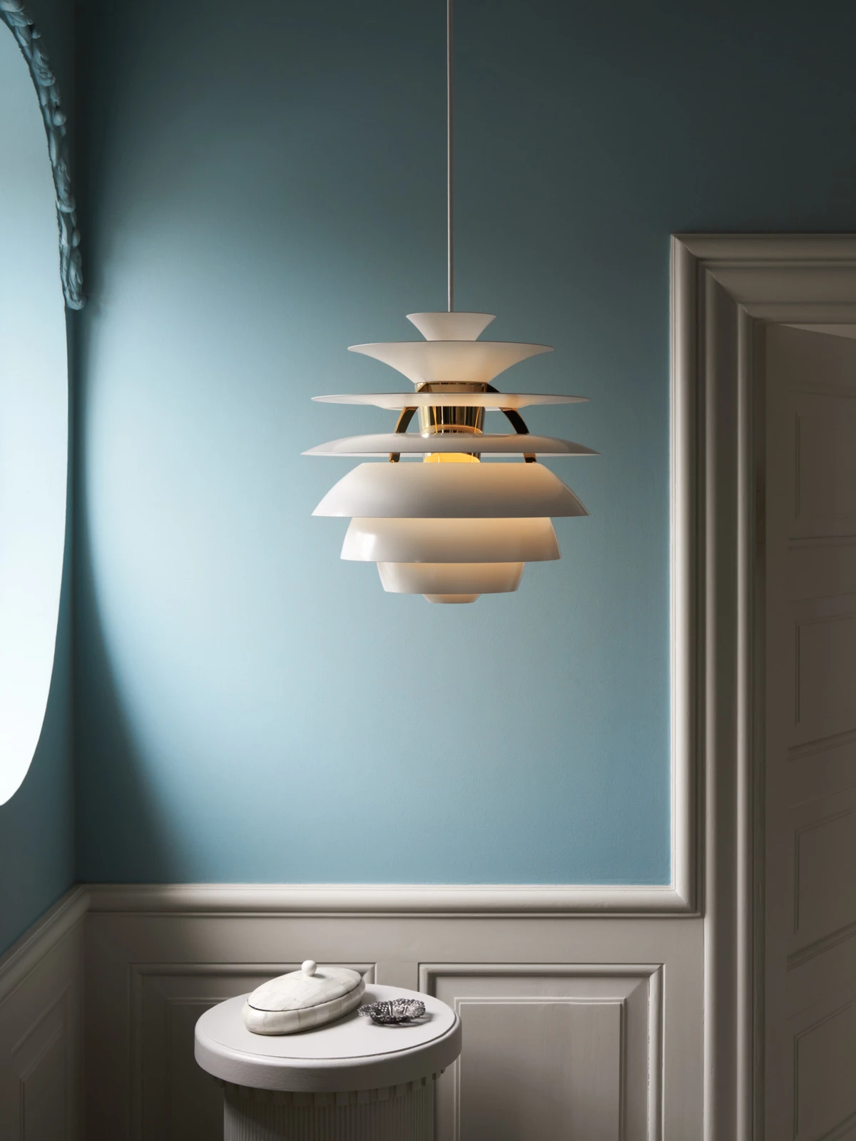 A white PH Snowball pendant hangs against a blue wall above a small round table. © 2026 Louis Poulsen.
