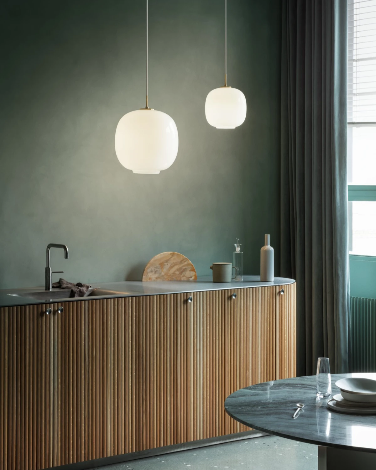 Twee VL 45 Radiohus hanglampen van opaalglas verlichten een kookeiland met een geribbelde houten voorkant. © 2026 Louis Poulsen.