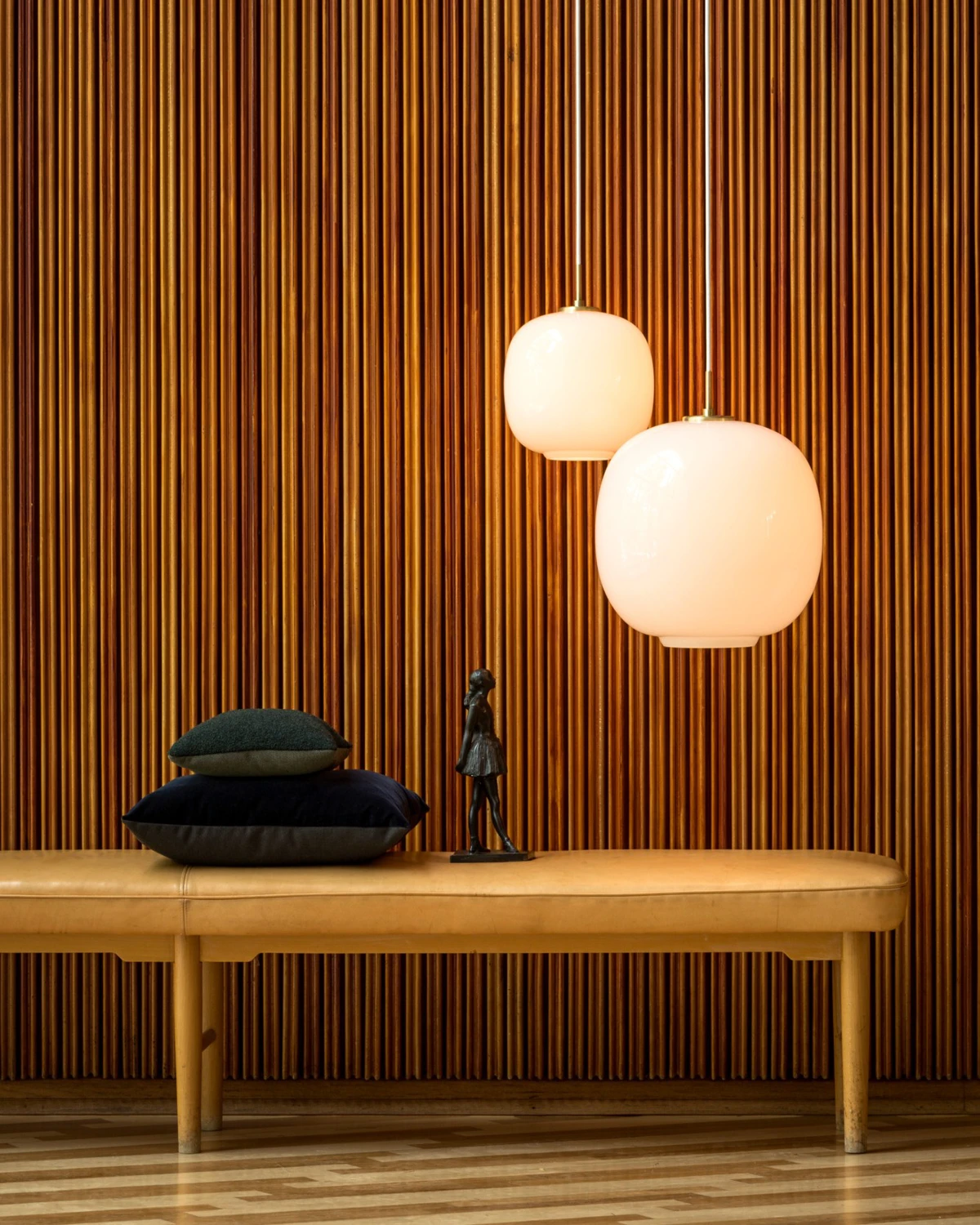 Twee VL 45 Radiohus hanglampen van wit opaalglas hangen boven een leren bank voor een wand met houten latten. © 2026 Louis Poulsen.