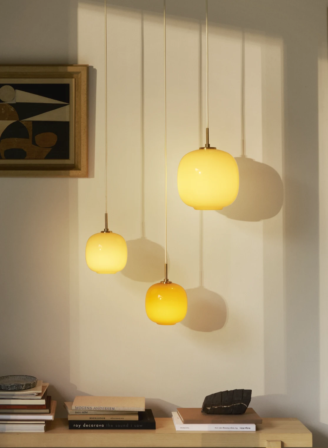 Drie VL 45 Radiohus hanglampen in warme gele en oranje tinten hangen boven een laag houten dressoir. © 2026 Louis Poulsen.