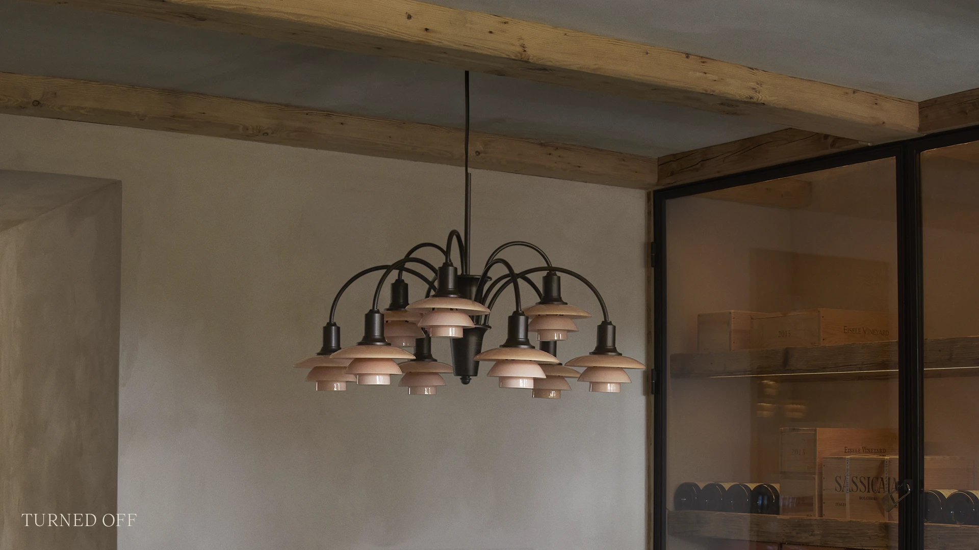 De PH 1/1 Chandelier Centenary Edition hangt uitgeschakeld in een ruimte met zichtbare houten balken en een glazen wand. © 2026 Louis Poulsen.
