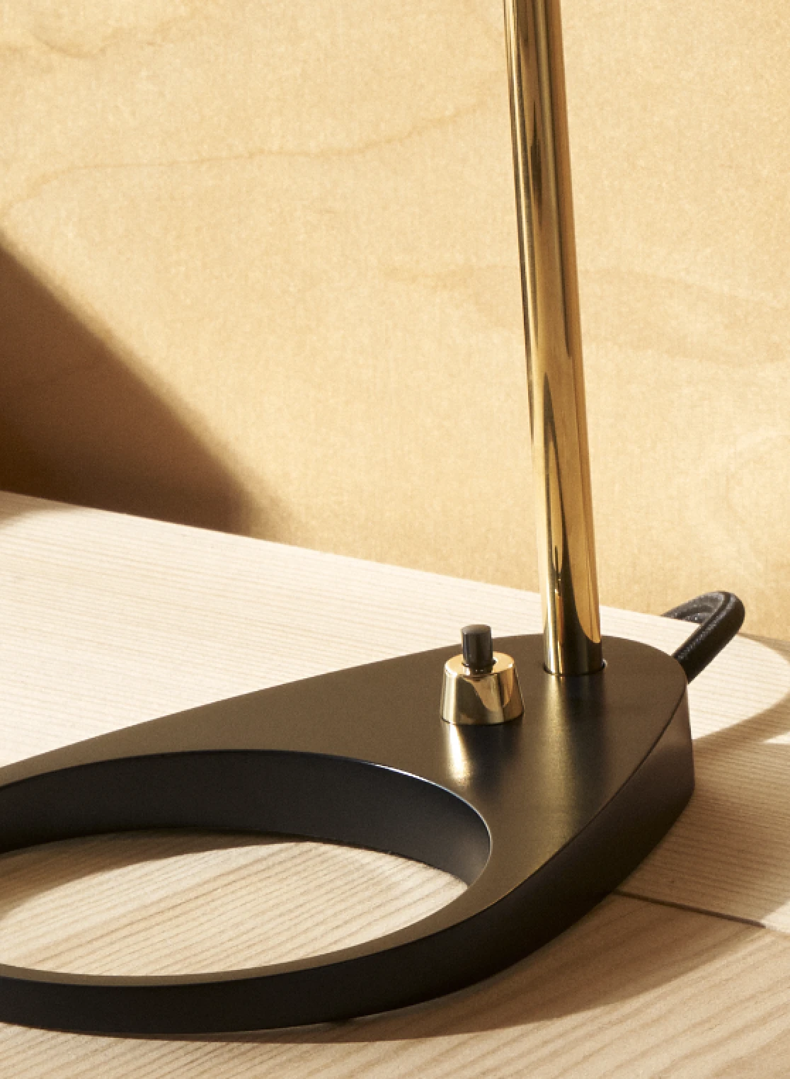 Dettaglio di una lampada da tavolo AJ Mini con base nera e stelo in ottone su un tavolo di legno chiaro. © 2026 Louis Poulsen.