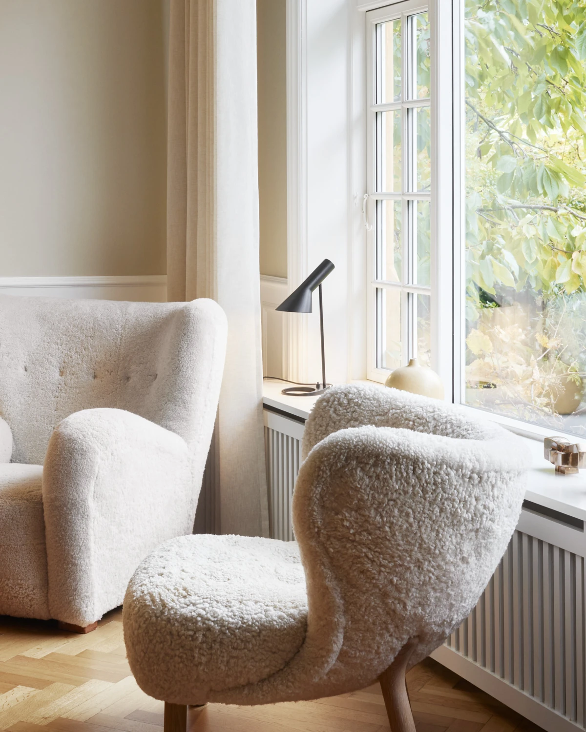 AJ Mini Table lamp in black on a windowsill beside cozy armchairs and natural light, © 2025 Louis Poulsen.