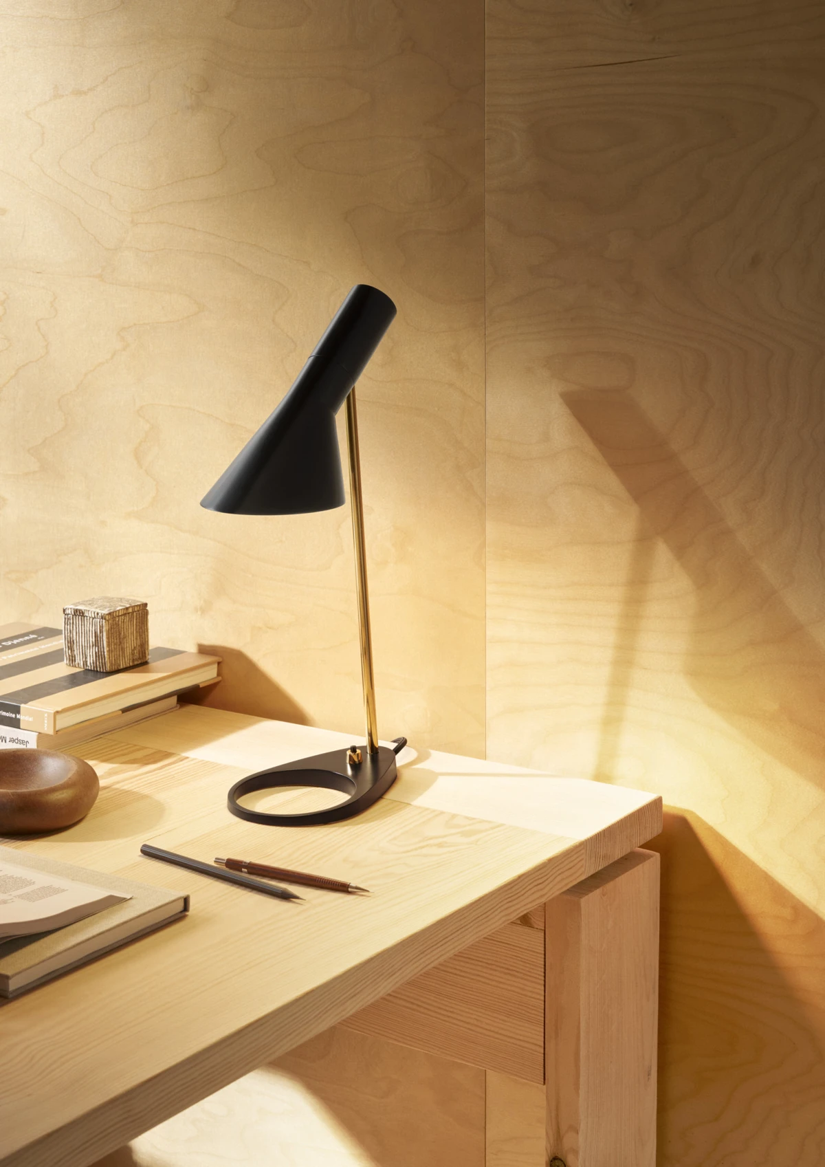 AJ Mini Table lamp in black and brass on a desk, soft lighting and wooden surroundings, © 2025 Louis Poulsen.