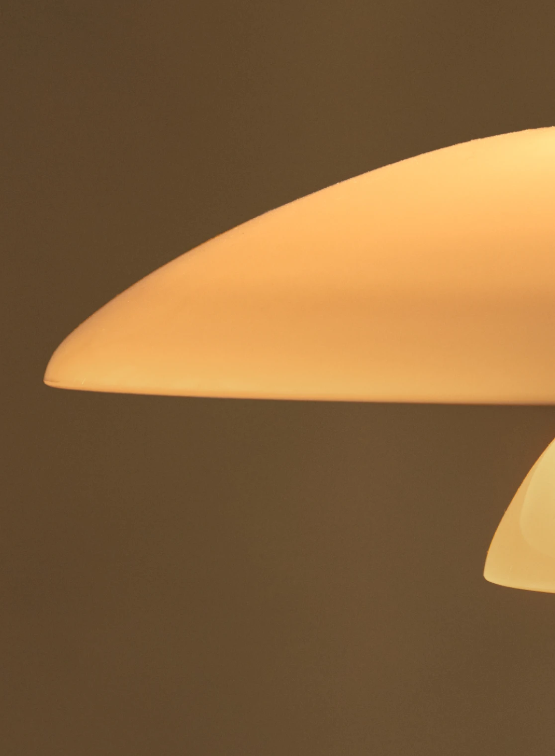 Close-up of a glowing PH 2/1 Table Lamp with cream-coloured shades against a brown background. © 2026 Louis Poulsen.