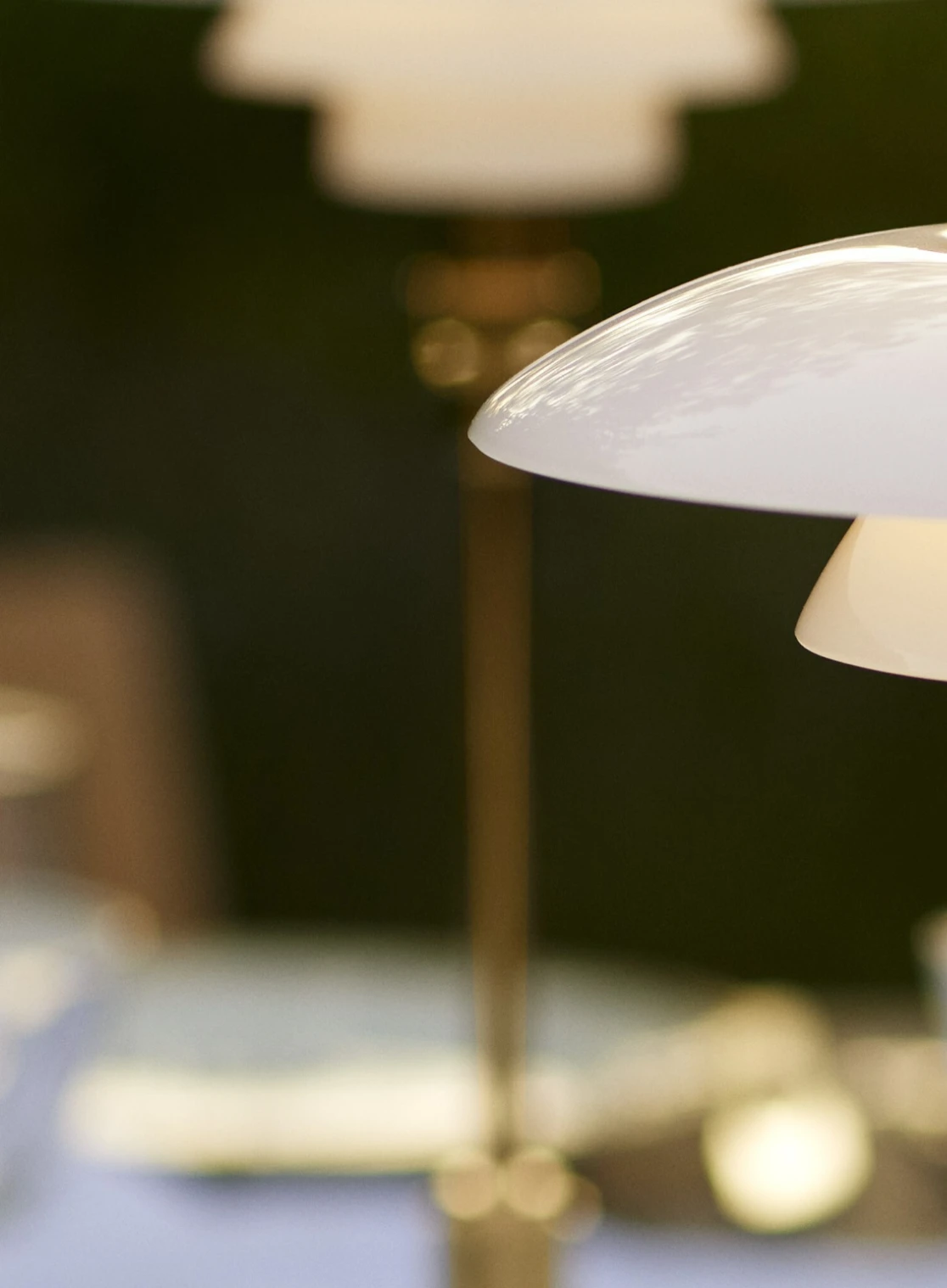 De draagbare PH 2/1 lamp van wit opaalglas met messingdetails is van dichtbij te zien in een warm verlicht interieur. © 2026 Louis Poulsen.