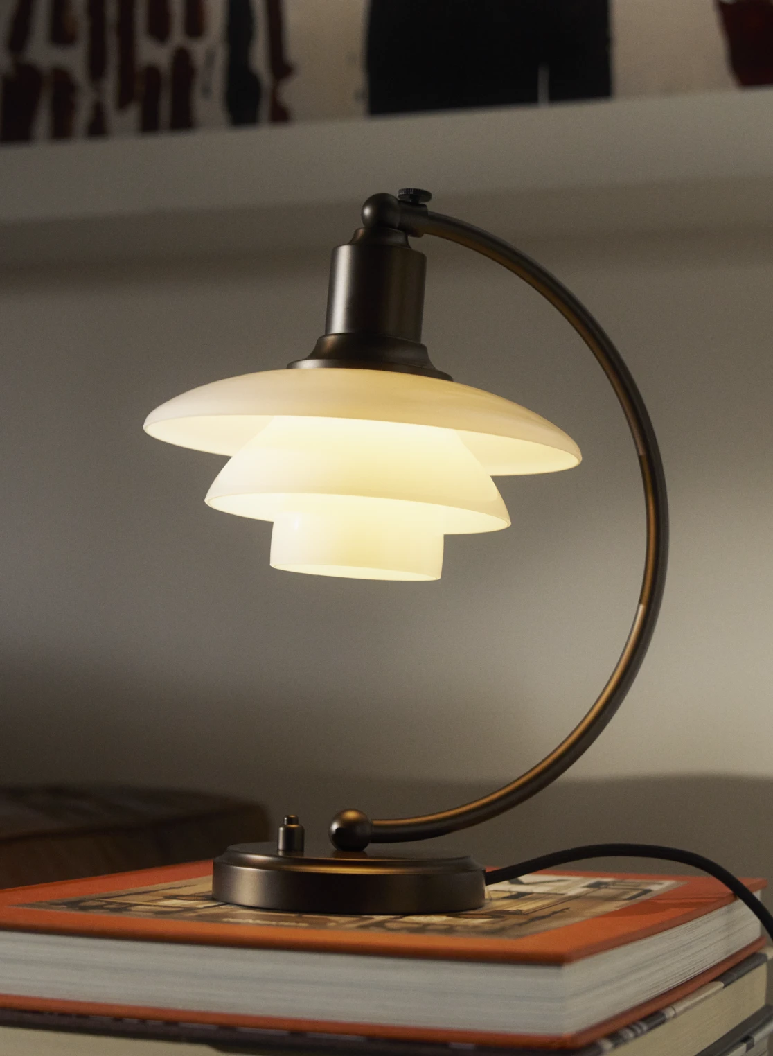 PH 2/2 Luna table lamp in aged brass with layered shades, resting on a stack of books