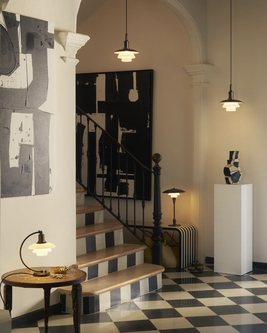 PH 2/2 Luna, PH 3/2 table lamp and PH 3/3 pendant lights in aged brass, complementing a stylish staircase setting, © 2025 Louis Poulsen.