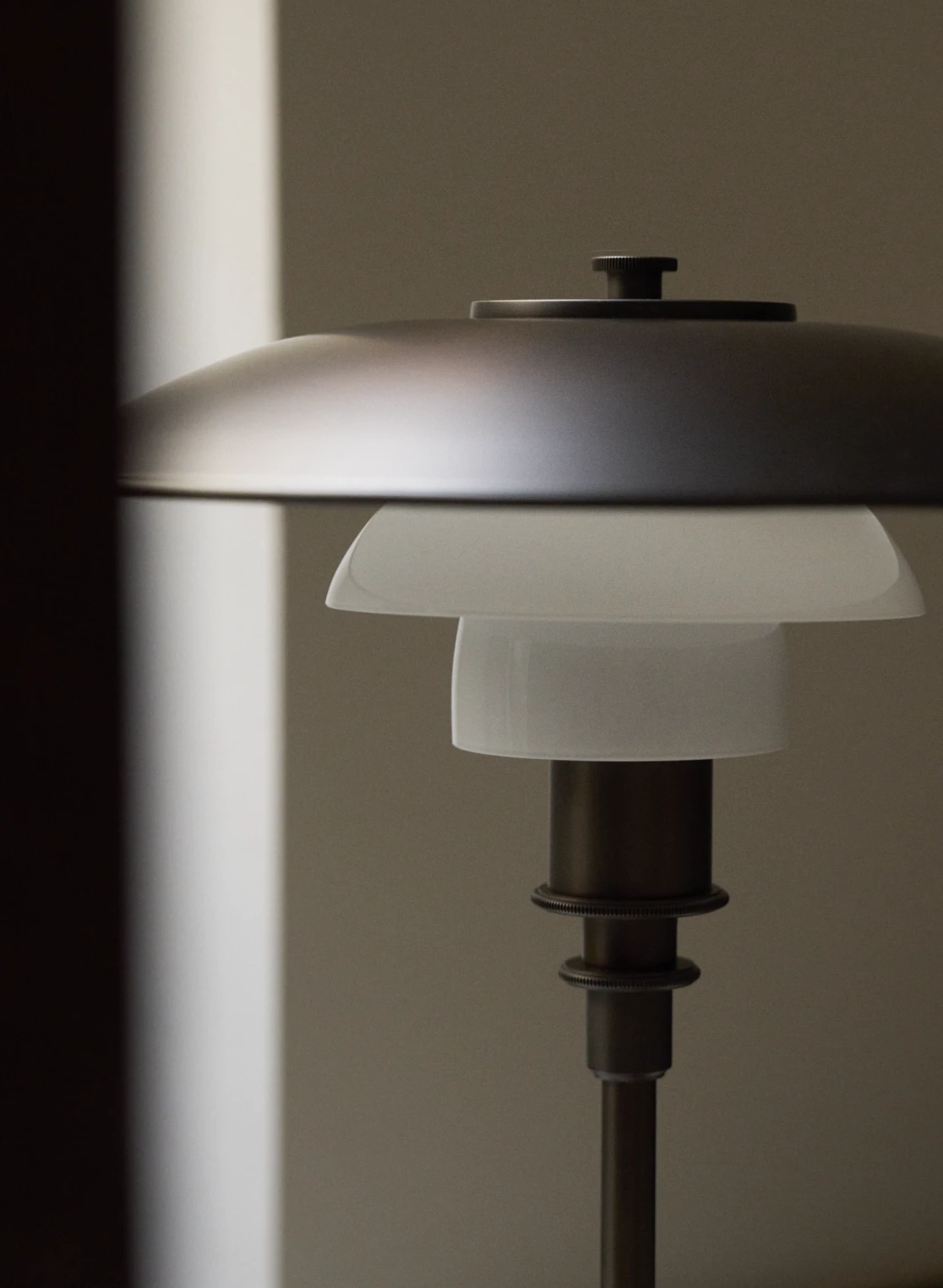 PH 3/2 Aged Brass table lamp in a warm, minimalist setting with a natural wood backdrop, © 2025 Louis Poulsen.