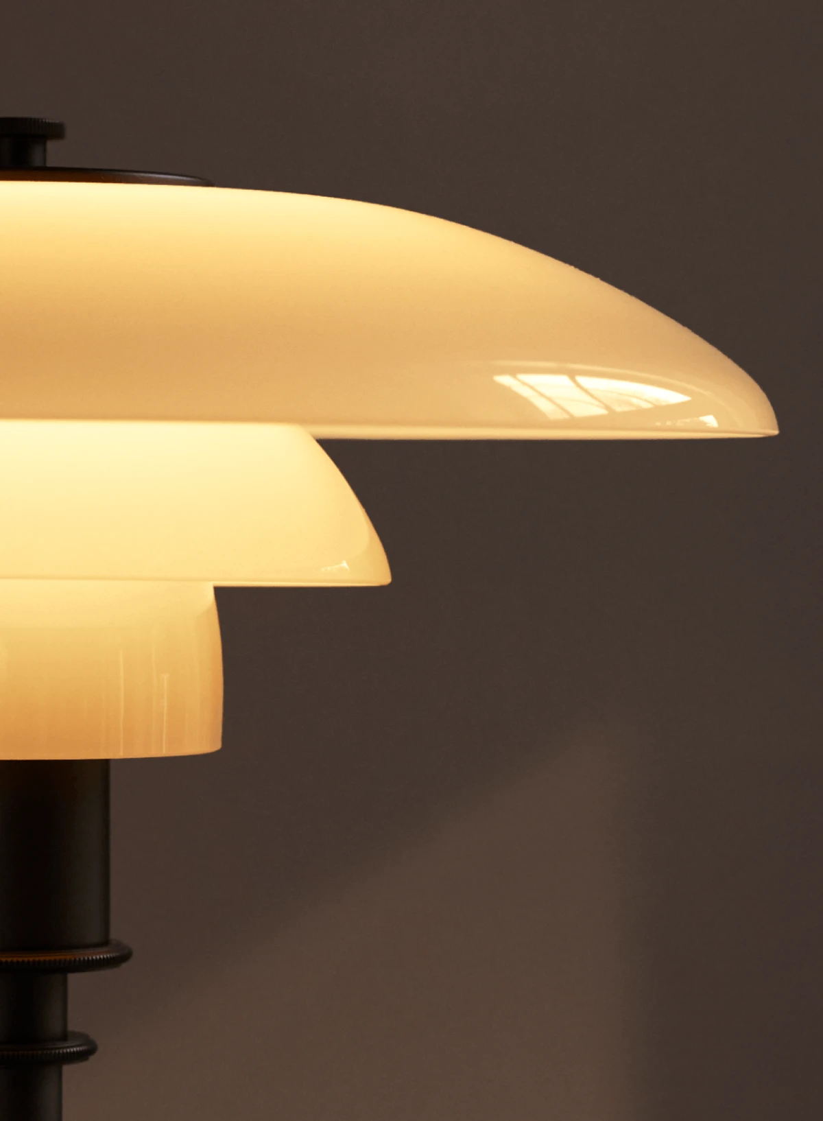 PH 3/2 bordlampe med opalhvide glasskærme lyser varmt mod en mørk baggrund. © 2026 Louis Poulsen.