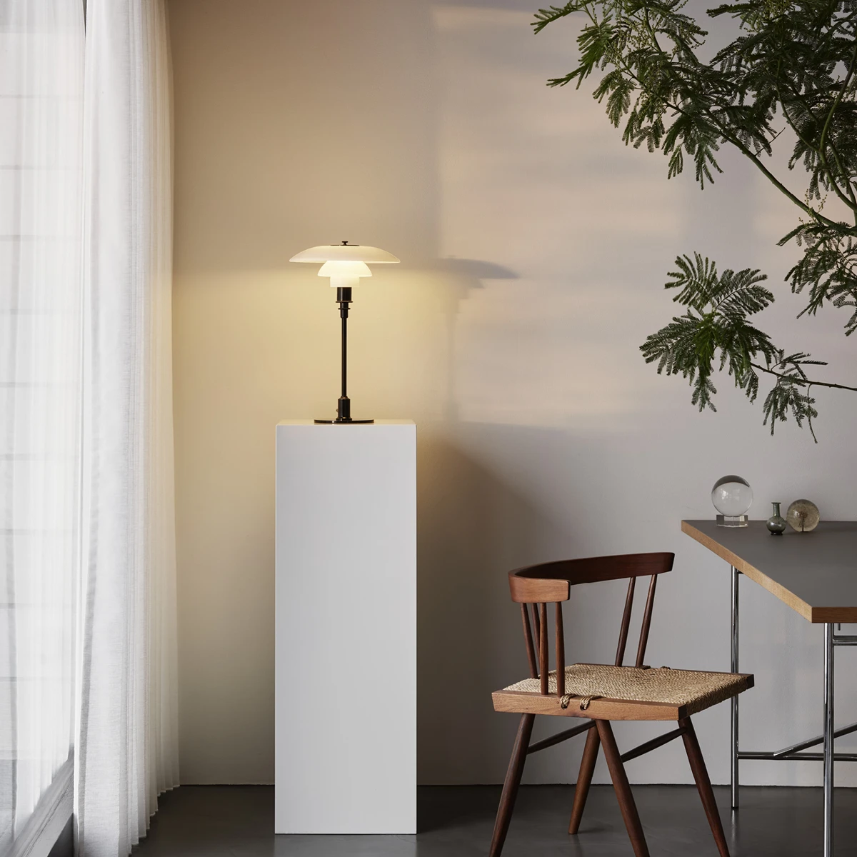 Die PH 3/2 Tischleuchte mit weißen Schirmen und schwarzem Gestell leuchtet neben einem Stuhl im Wohnraum. © 2026 Louis Poulsen.