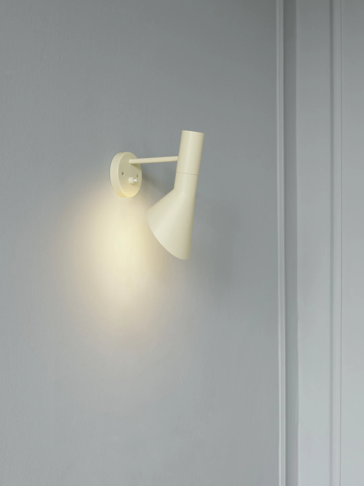 AJ Wall lamp in soft lemon on a grey wall, casting warm light, © 2025 Louis Poulsen.