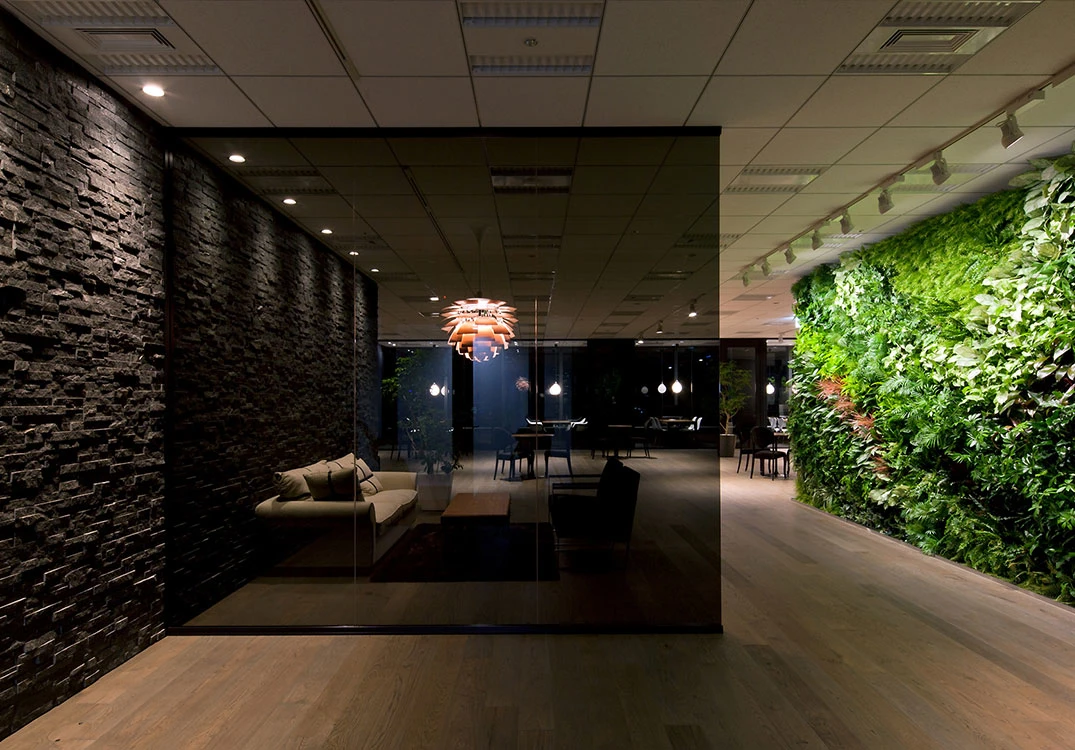 A PH Artichoke pendant glows in a modern lounge with a dark stone wall and a lush green wall. © 2026 Louis Poulsen.