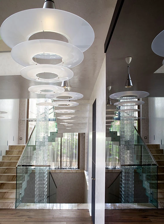 Enigma Pendant lights with layered white shades hang above a staircase with glass balustrades. © 2026 Louis Poulsen.
