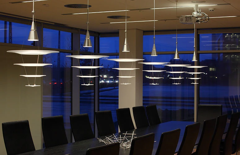 Enigma pendants hang above a long conference table in a modern meeting room with large windows. © 2026 Louis Poulsen.