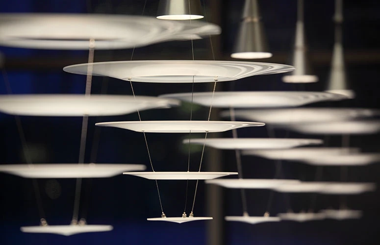White Enigma Pendants hang at different heights in a dark interior. © 2026 Louis Poulsen.