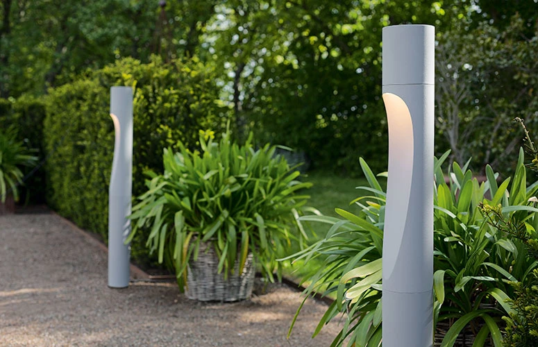 Grey Flindt Bollards glow beside a garden path bordered by lush greenery. © 2026 Louis Poulsen.