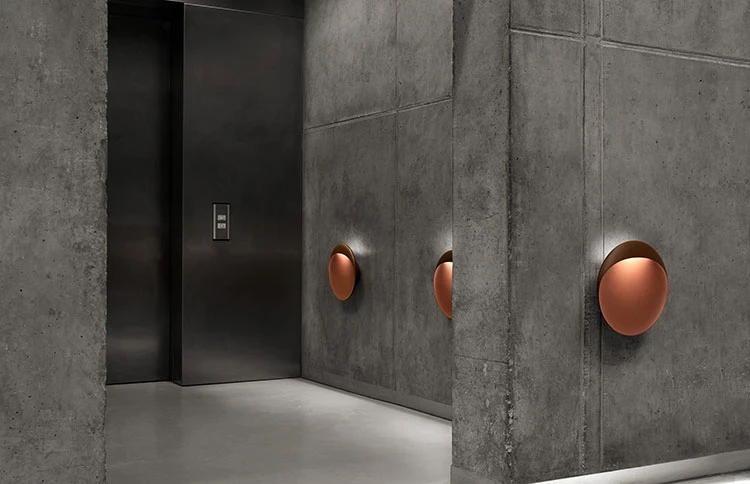 Corten-finished Flindt Wall Lamps cast a warm glow across the concrete walls of a modern corridor. © 2026 Louis Poulsen.