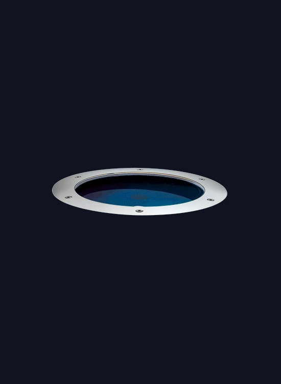 A round recessed Louis Poulsen luminaire with a silver rim and blue-tinted glass against a dark background. © 2026 Louis Poulsen.