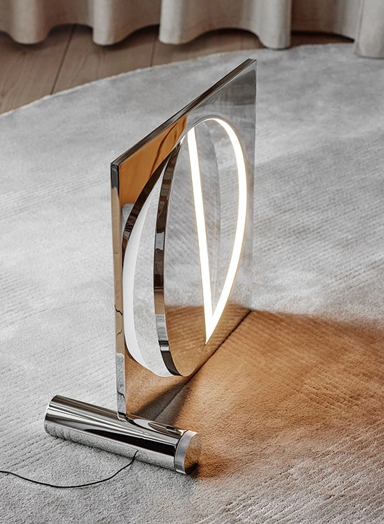 The chrome Moonsetter floor lamp stands on a pale rug, casting a warm glow. © 2026 Louis Poulsen.