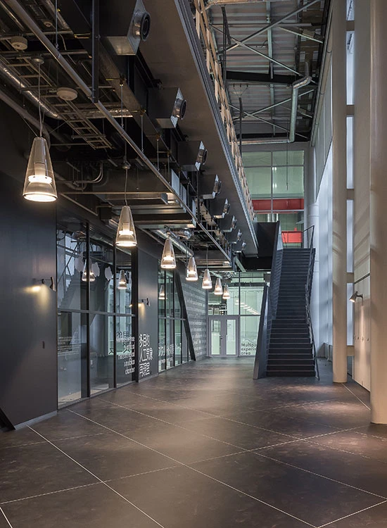 Toldbod Glass Pendants illuminate a modern corridor with dark flooring, glass walls and a staircase. © 2026 Louis Poulsen.