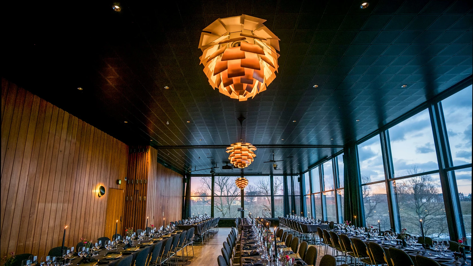 PH Artichoke pendants glow above set tables in the glass-walled dining room at Langelinie Pavillonen. © 2026 Louis Poulsen.