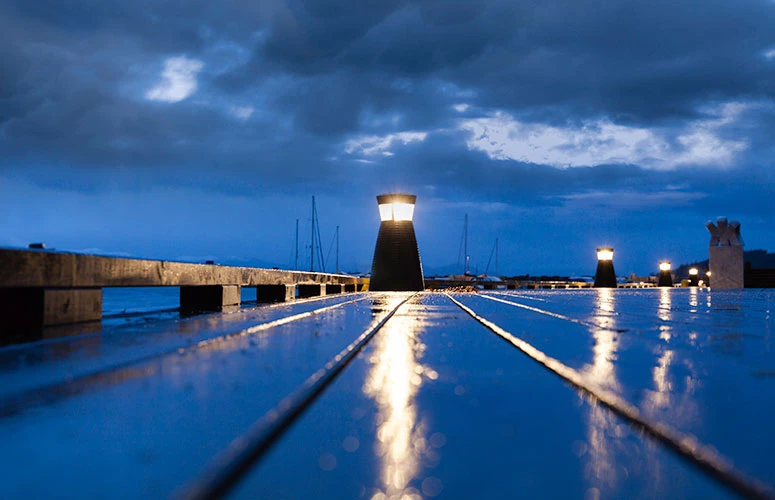 Louis Poulsen bollard lights illuminate a wet harbour promenade beneath a deep blue evening sky. © 2026 Louis Poulsen.