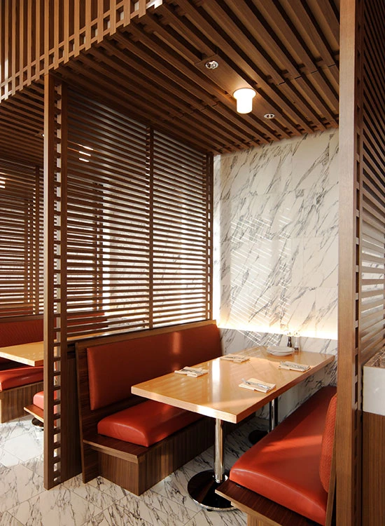 A Ballerup ceiling lamp lights a dining booth with red leather seats, timber slats and marble surfaces. © 2026 Louis Poulsen.