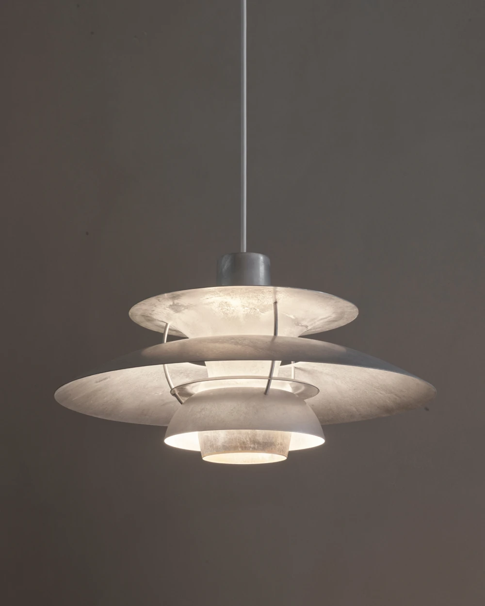 De PH 5 Retake hanglamp met gloeiende, gestructureerde kappen tegen een donkere wand. © 2026 Louis Poulsen.