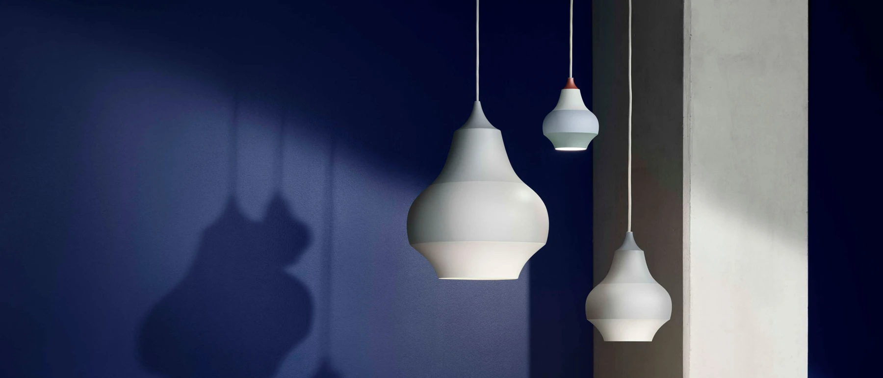 White Cirque Pendants in different sizes hang against a deep blue wall. © 2026 Louis Poulsen.