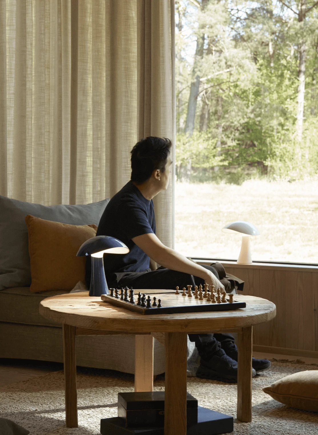 En mörkblå och en vit Panthella 160 Portable Lamp står bredvid ett schackbräde på ett soffbord av trä. © 2026 Louis Poulsen.