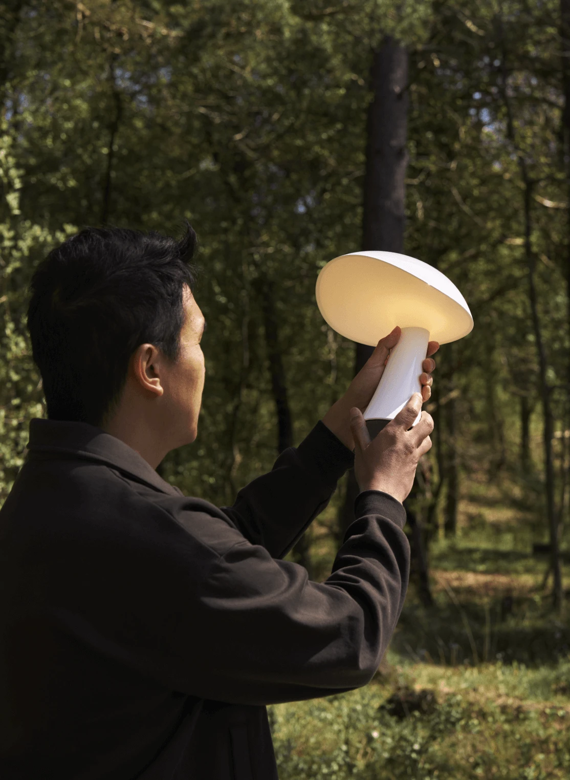 En vit Panthella 250 Portable Lamp lyser när en person håller den i en skog. © 2026 Louis Poulsen.
