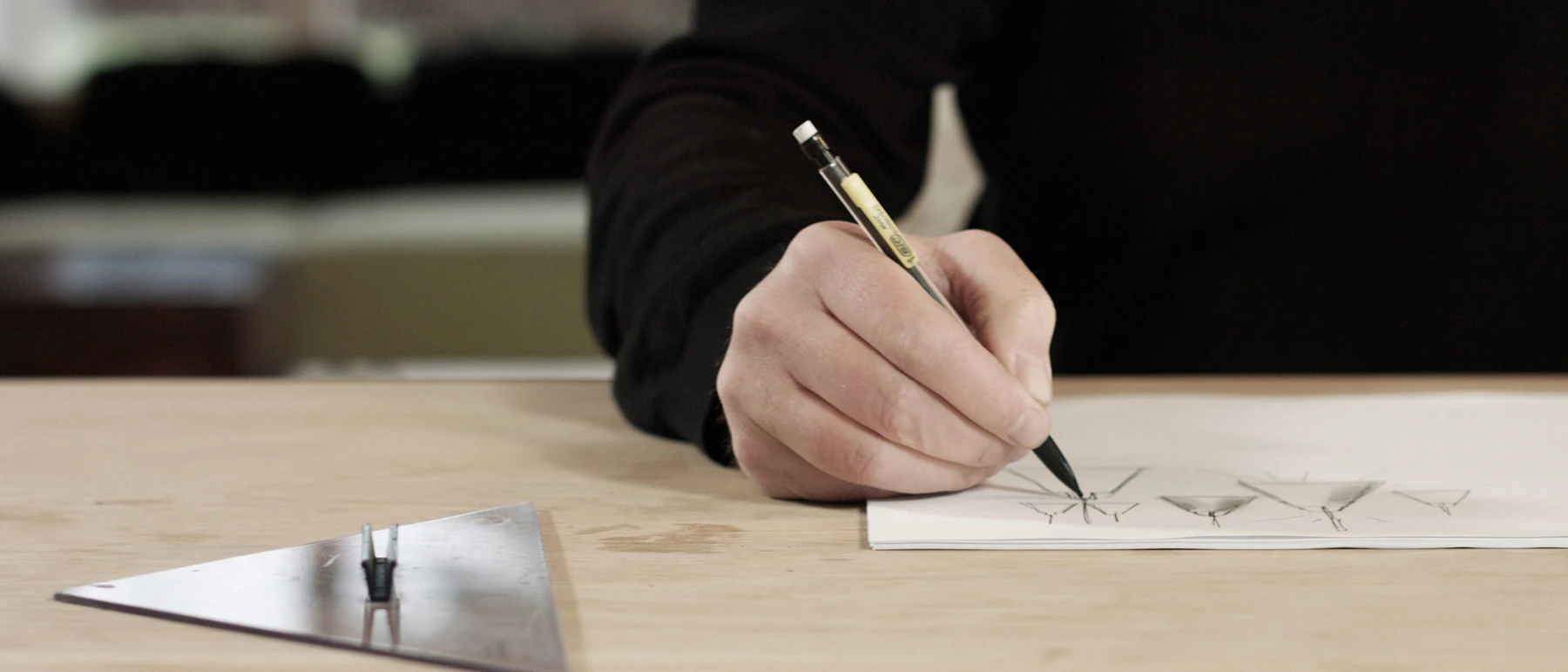 Mads Ølgård sketches the Above Pendant at a wooden drafting table. © 2026 Louis Poulsen.