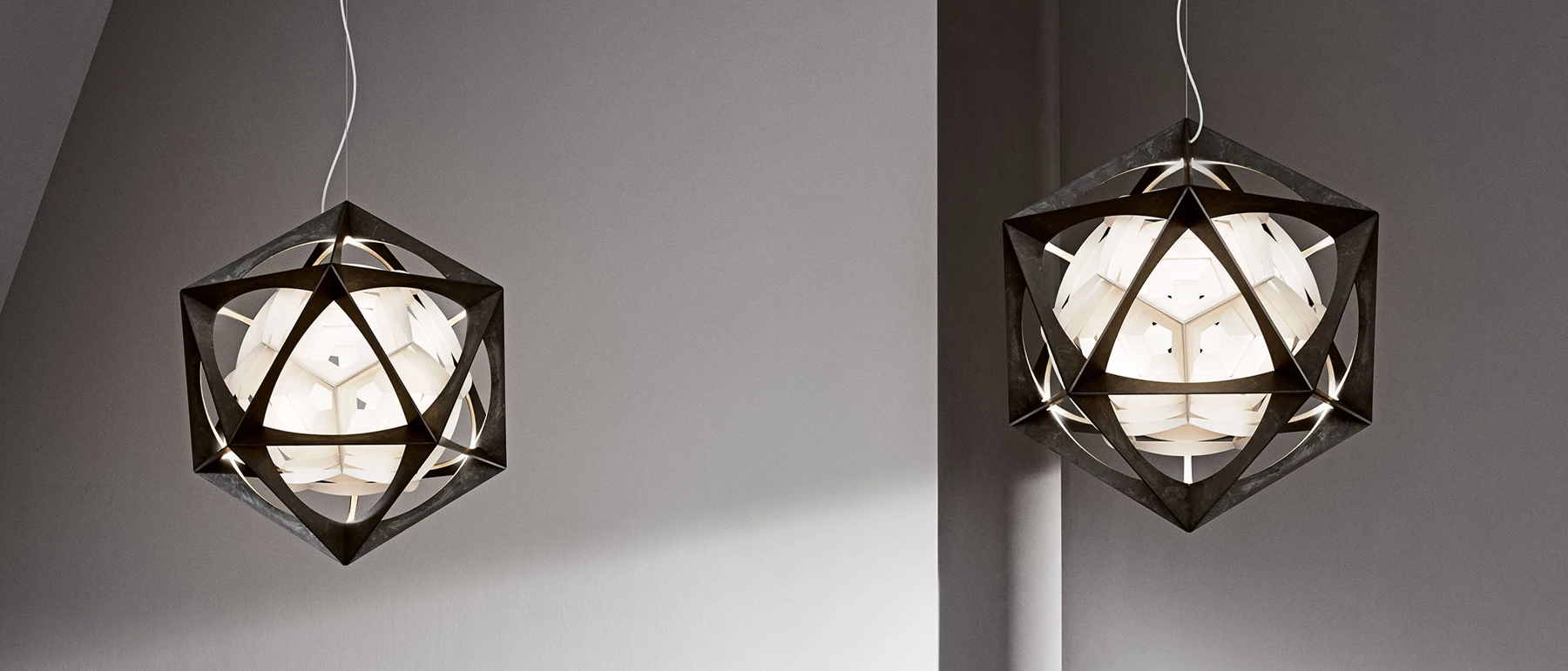 To OE Quasi-pendler med mørke geometriske metalrammer og lysende hvide skærme mod en grå væg. © 2026 Louis Poulsen.