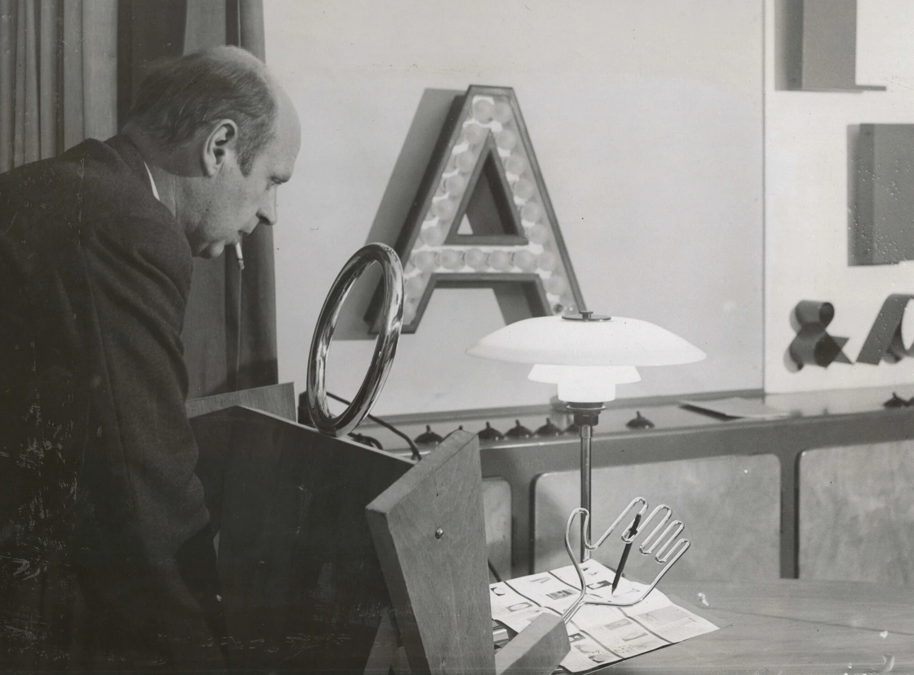 Poul Henningsen bestudeert vroege PH tafellamp in showroom, © 2025 Louis Poulsen.