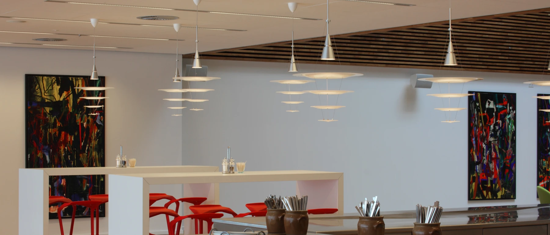 Enigma Pendants hang above a restaurant with red chairs and colourful paintings. © 2026 Louis Poulsen.