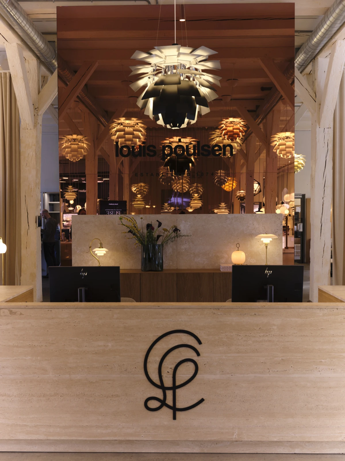 PH Artichoke pendants illuminate the Louis Poulsen showroom in Copenhagen, behind a reception desk of light stone. © 2026 Louis Poulsen.