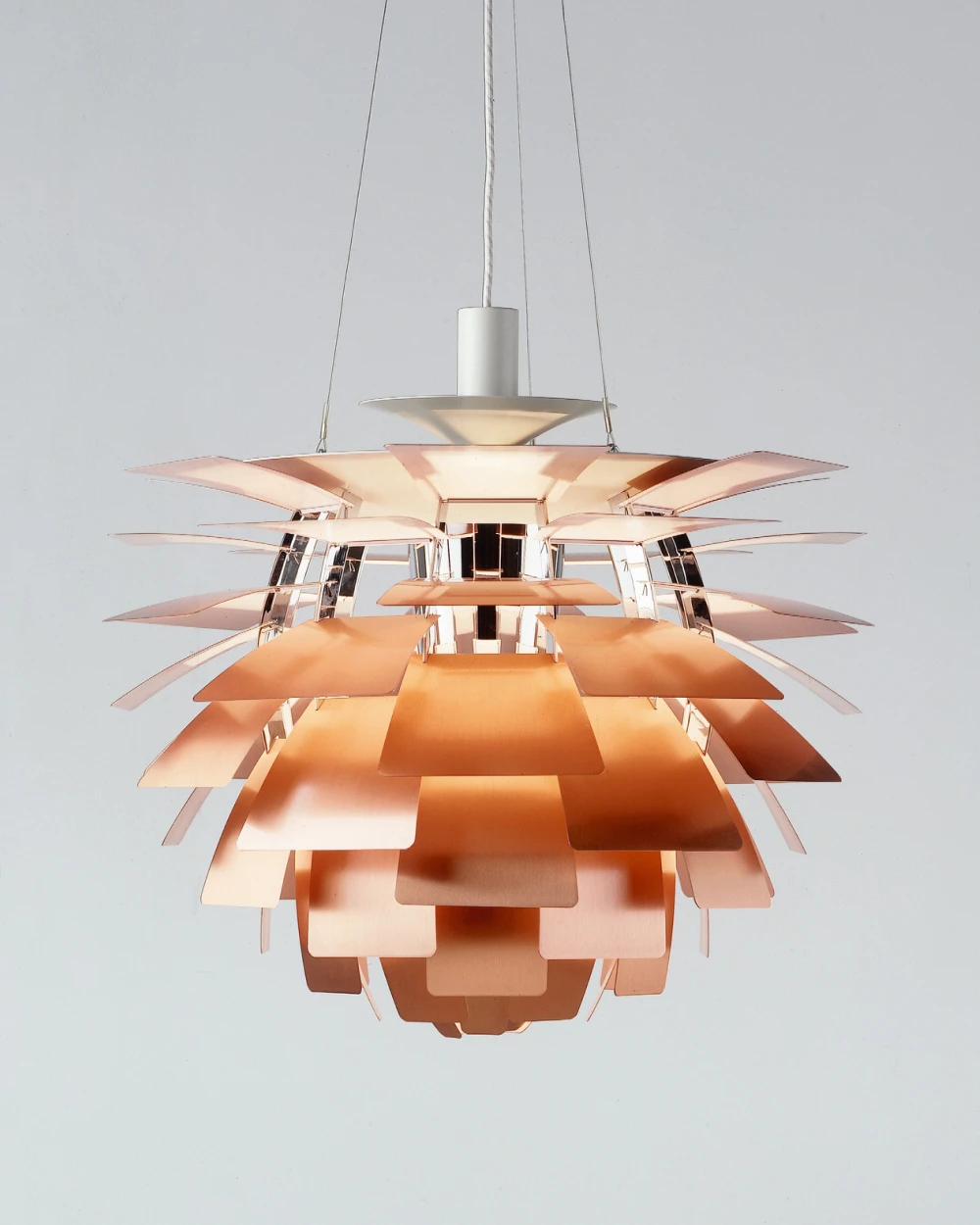 Een koperkleurige PH Artichoke hanglamp straalt warm licht uit tegen een lichte, neutrale achtergrond. © 2026 Louis Poulsen.
