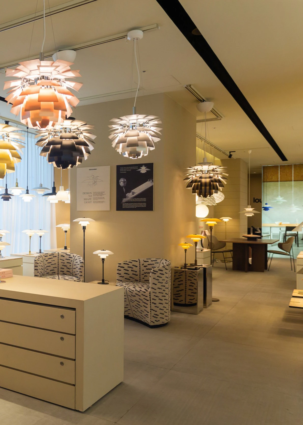 PH Artichoke-pendels in verschillende uitvoeringen hangen in de Louis Poulsen-showroom tussen tafel- en vloerlampen. © 2026 Louis Poulsen.