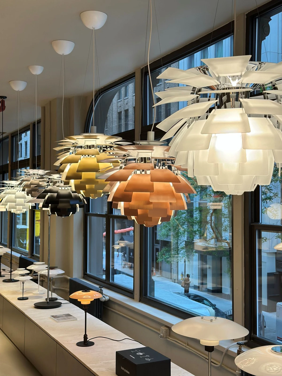 PH Artichoke hanglampen in wit, koper en metaal hangen in een showroom met grote ramen. © 2026 Louis Poulsen.