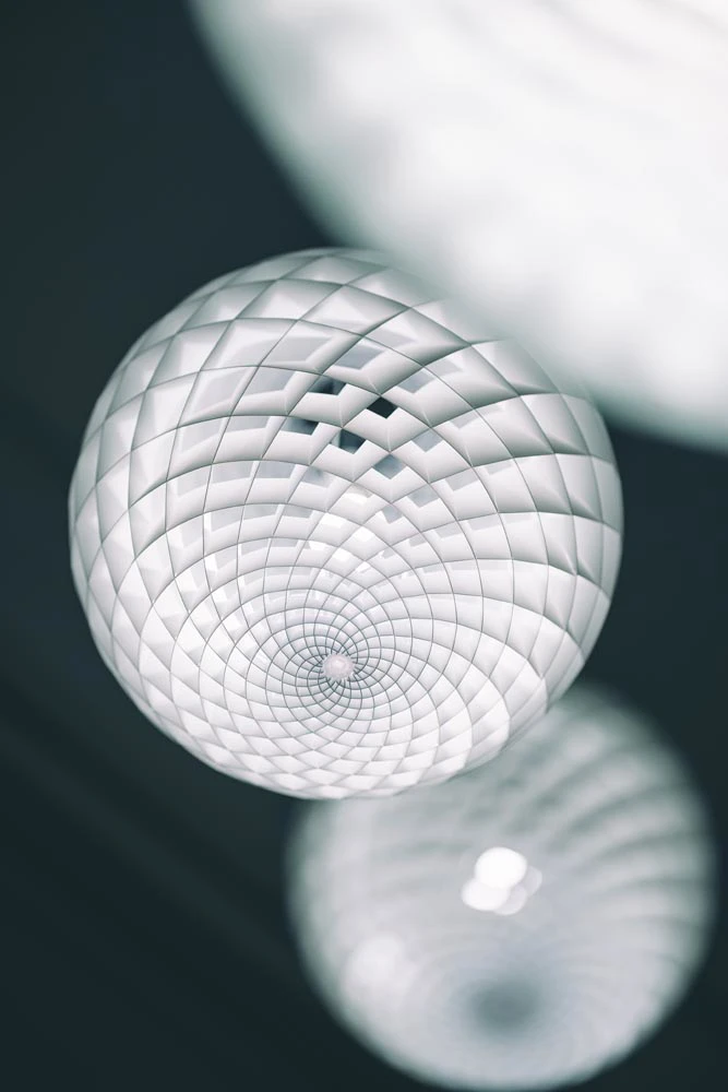 A white Patera Pendant hangs in the Oslo showroom, its intricate spiral shade shown in close-up. © 2026 Louis Poulsen.