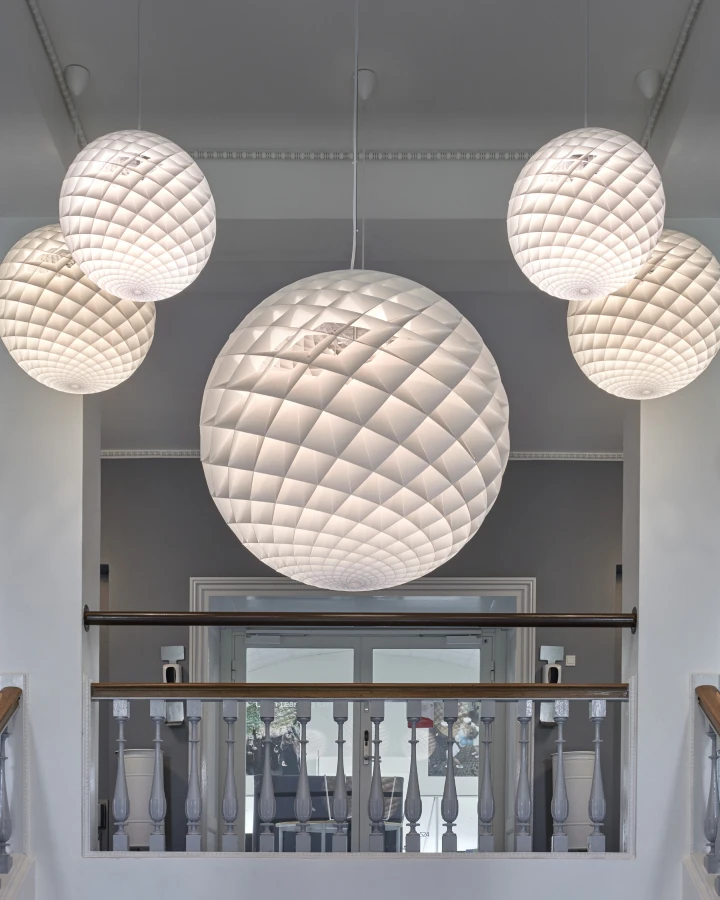Vijf witte Patera pendels in verschillende formaten hangen boven een overloop met balustrade. © 2026 Louis Poulsen.