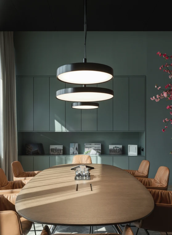 Drie zwarte LP Grand-hanglampen in verschillende formaten hangen boven een lange houten tafel in een moderne vergaderruimte. © 2026 Louis Poulsen.