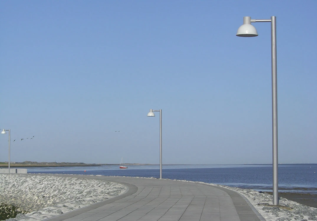 Albertslund Maxi Post lights line a paved promenade beside the water on Juist. © 2026 Louis Poulsen.