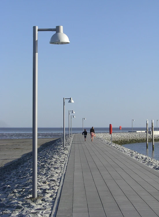 Albertslund Maxi Post lights line a wooden pier on Juist, bordered by rocks with the sea beyond. © 2026 Louis Poulsen.