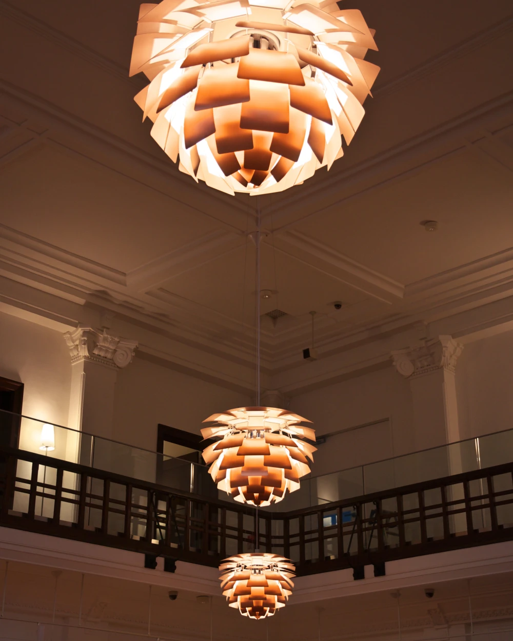 Drie verlichte PH Artichoke hanglampen hangen op verschillende hoogtes in een historisch gebouw met balkon. © 2026 Louis Poulsen.