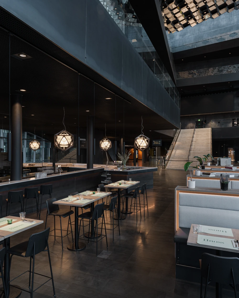 Patera Pendant-hanglampen verlichten de tafels in restaurant Hnoss, te midden van donkere vlakken en beton. © 2026 Louis Poulsen.