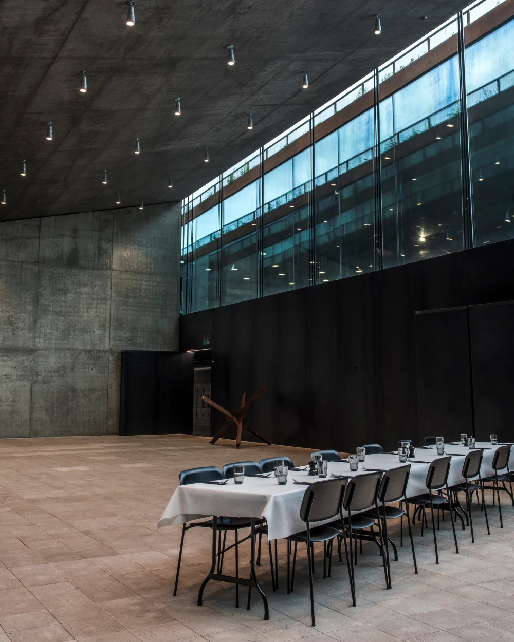 LP Xperi-plafondlampen verlichten een lange tafel in de betonnen hal van het Tirpitz Museum met grote glaspartijen. © 2026 Louis Poulsen.