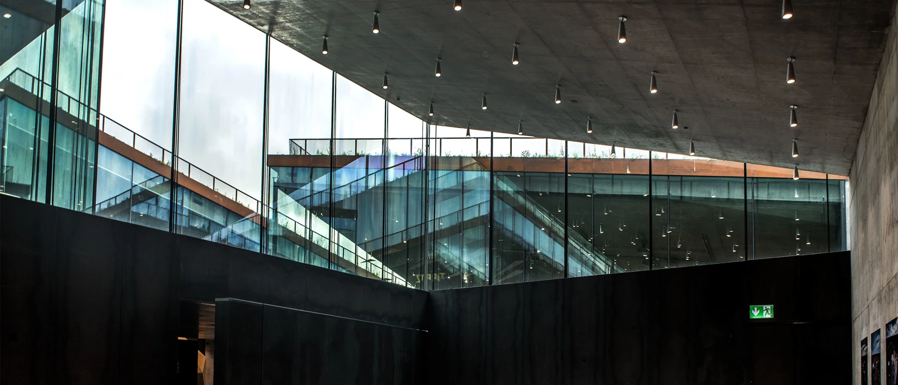 LP Xperi ceiling lights illuminate a dark concrete gallery at Tirpitz Museum, alongside expansive glass walls. © 2026 Louis Poulsen.